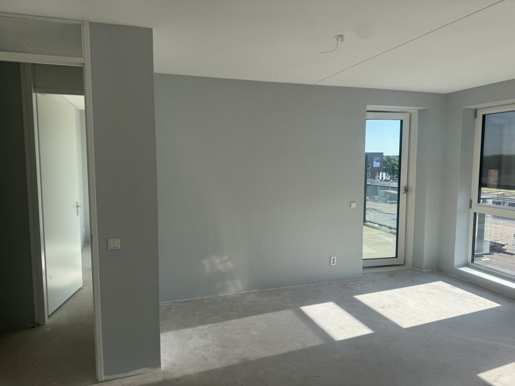 Nieuw appartement met kale betonvloer, lichtgrijs gesausde wanden en een deur naar het balkon