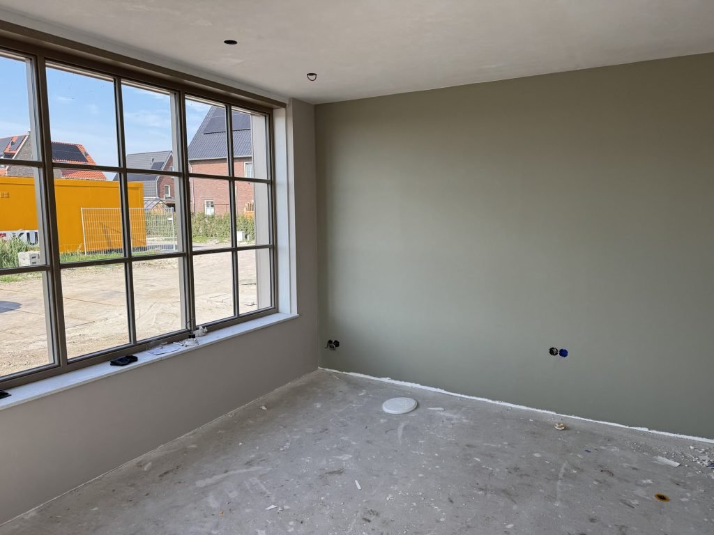 Kamer in een nieuwbouwwoning met een gesausde wand in grijsgroen en een groot raam met roedes