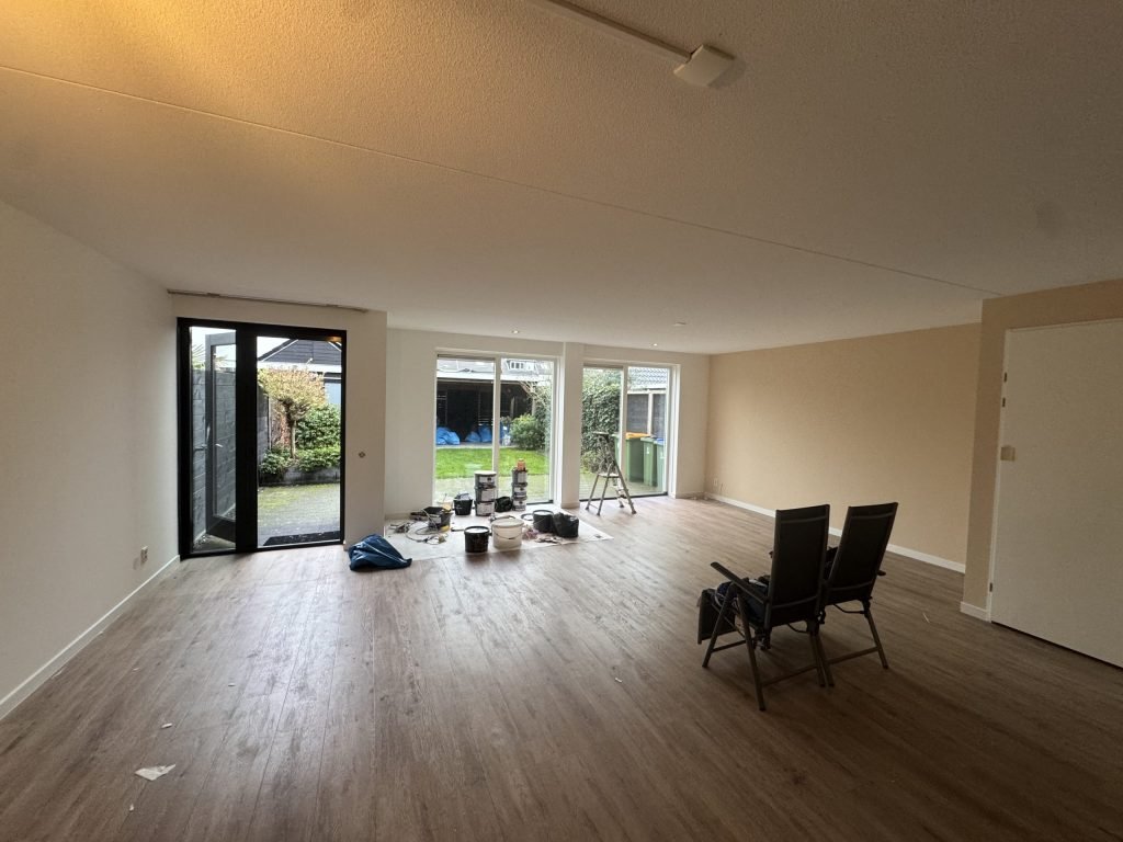 Ruime woonkamer met licht gesausde wanden, een houten vloer en tuindeuren